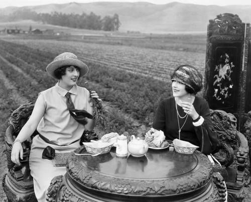 1920's photo of 2 women sipping tea in a field.